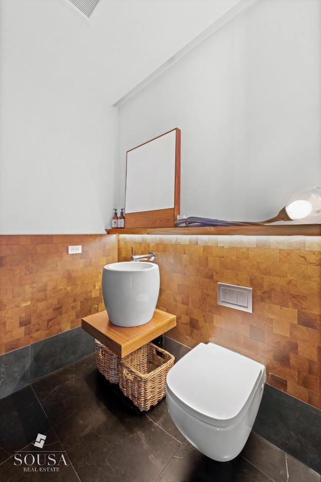 half bath featuring toilet, tile walls, tile patterned floors, a wainscoted wall, and a sink