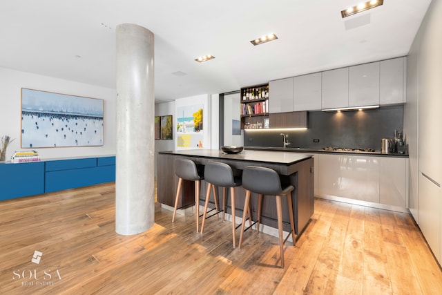 kitchen featuring decorative columns, dark countertops, a breakfast bar, modern cabinets, and light wood finished floors