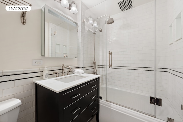 bathroom featuring toilet, tile walls, combined bath / shower with glass door, and vanity
