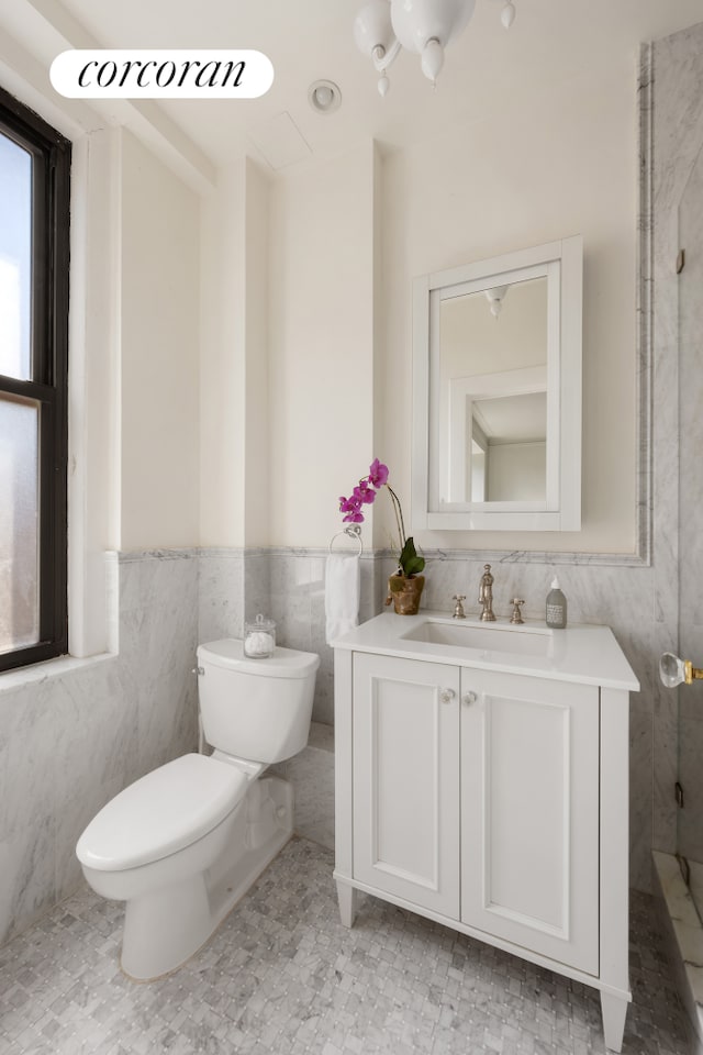 bathroom with tile walls, a wainscoted wall, vanity, and toilet