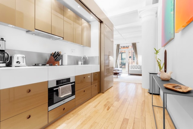 kitchen featuring light wood-style floors, stainless steel oven, light countertops, under cabinet range hood, and stovetop