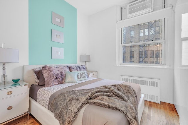 bedroom featuring a wall mounted air conditioner, radiator, and hardwood / wood-style floors