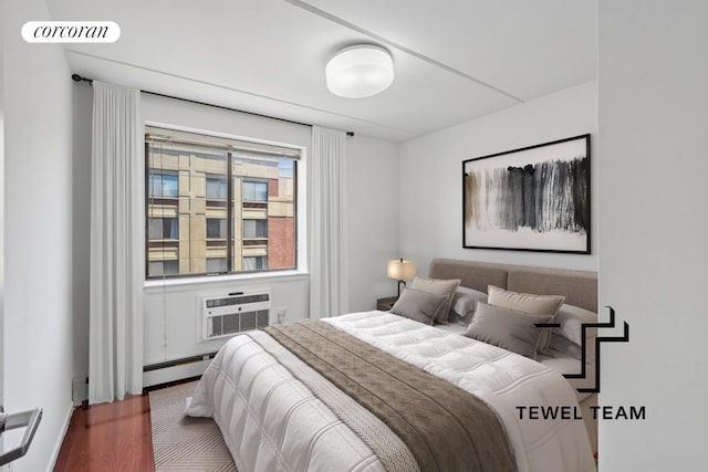 bedroom with a wall mounted air conditioner, a baseboard heating unit, wood finished floors, and visible vents