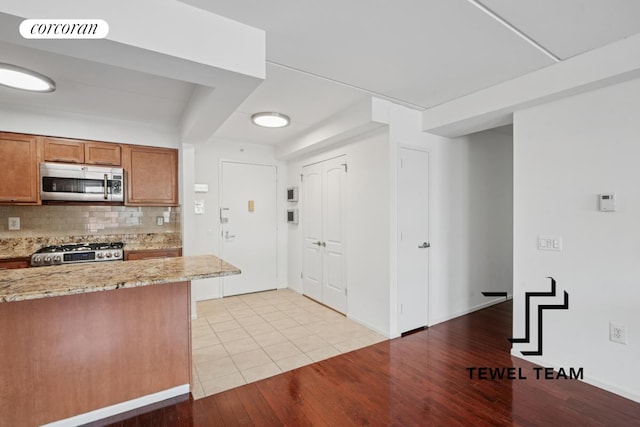 kitchen with appliances with stainless steel finishes, tasteful backsplash, brown cabinets, light stone counters, and light wood-style flooring