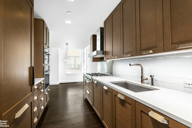 kitchen featuring dark wood-type flooring, light countertops, wall chimney exhaust hood, tasteful backsplash, and a sink