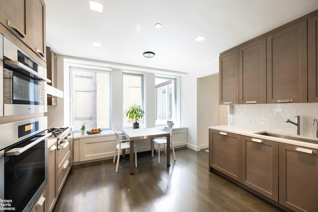 kitchen with a sink, backsplash, dark wood-style floors, and light countertops