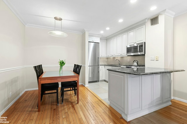 211 W 71st St Unit 2C, New York City, NY 10023 - kitchen with appliances with stainless steel finishes, light wood-style flooring, backsplash, white cabinetry, and ornamental molding