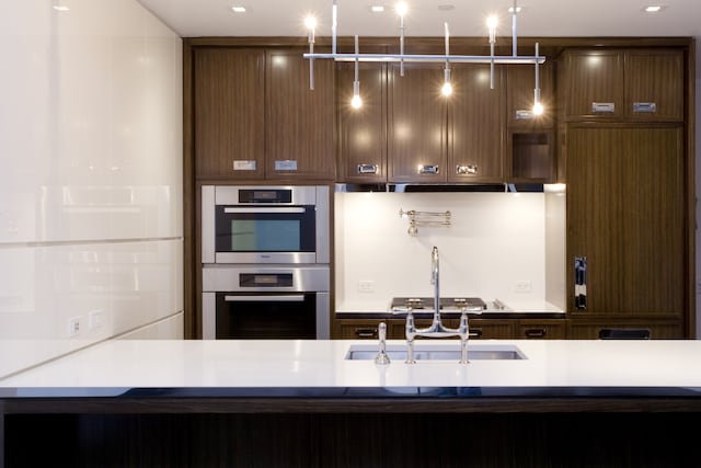 kitchen with stainless steel double oven, a sink, dark brown cabinets, and light countertops