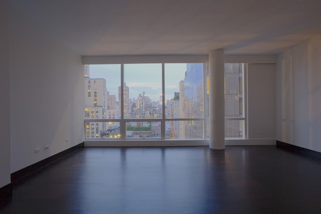 unfurnished room with baseboards, a city view, and dark wood-type flooring