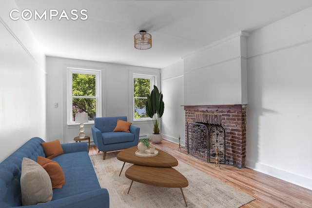 living area featuring baseboards, a baseboard radiator, a brick fireplace, and wood finished floors