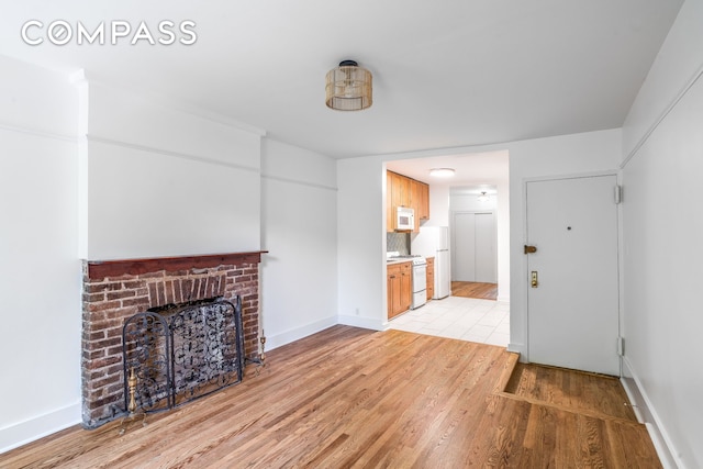 unfurnished living room with light wood-type flooring, baseboards, and a brick fireplace