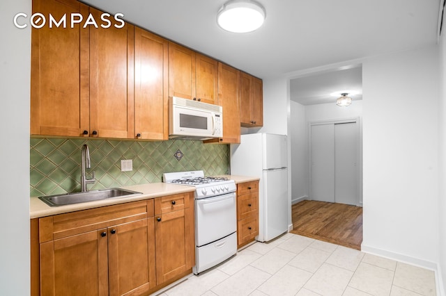 kitchen with brown cabinetry, decorative backsplash, white appliances, light countertops, and a sink