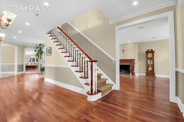 stairs with crown molding, recessed lighting, wood finished floors, and a fireplace