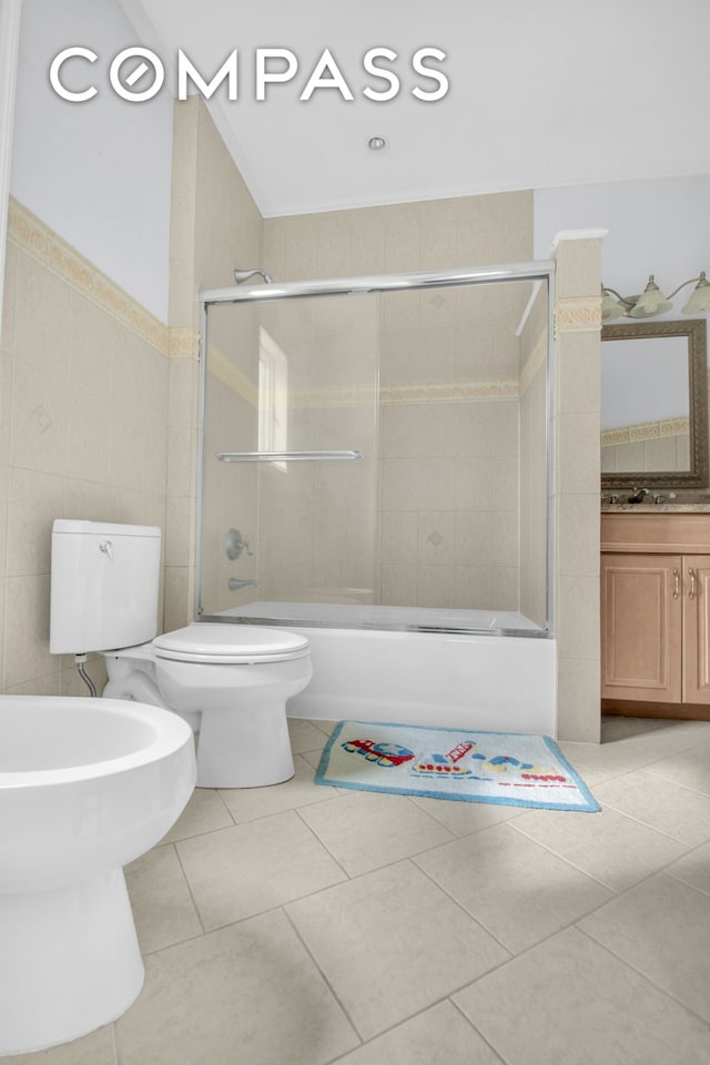 bathroom featuring combined bath / shower with glass door, tile patterned floors, toilet, and tile walls