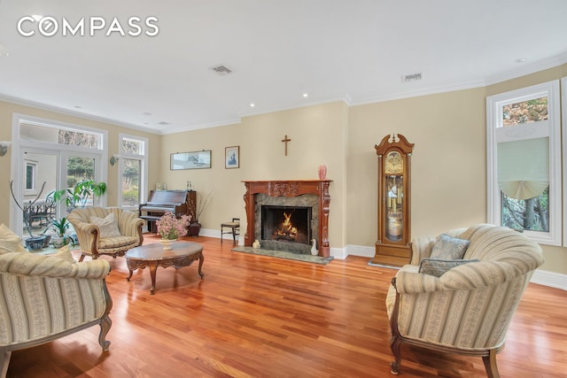 living room featuring crown molding, visible vents, baseboards, light wood-type flooring, and a high end fireplace