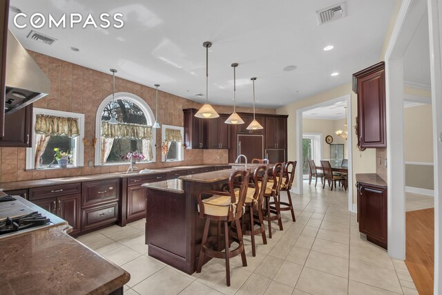 kitchen with visible vents, a center island, wall chimney exhaust hood, backsplash, and hanging light fixtures