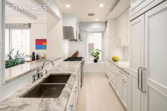 kitchen featuring wall chimney range hood, white cabinets, a wealth of natural light, and a sink