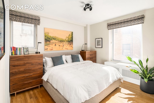 bedroom featuring radiator heating unit, multiple windows, and wood finished floors