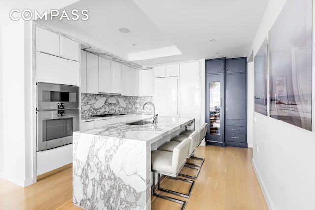 10 Riverside Blvd Unit 28C, New York City, NY 10069 - kitchen with a sink, white cabinetry, light wood finished floors, and decorative backsplash