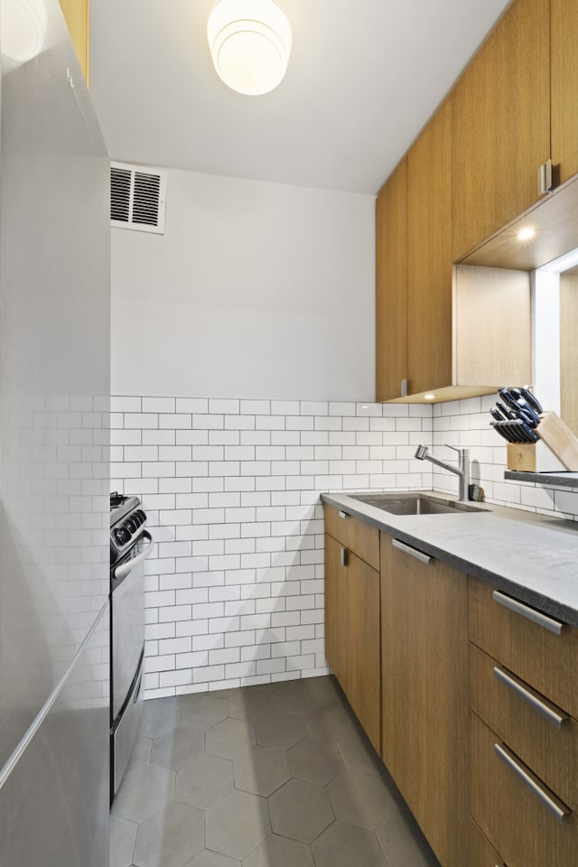 kitchen featuring visible vents, tile walls, dark tile patterned floors, stainless steel range oven, and a sink