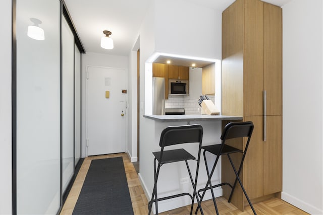 kitchen with brown cabinetry, decorative backsplash, baseboards, a breakfast bar area, and light countertops