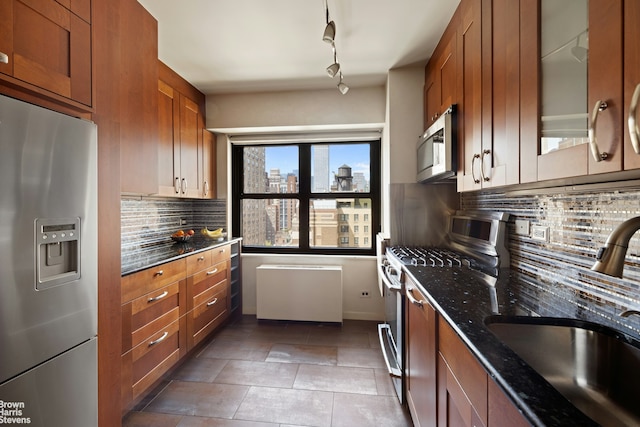 kitchen with a sink, dark stone counters, appliances with stainless steel finishes, and brown cabinets