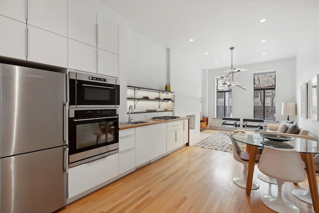 kitchen featuring appliances with stainless steel finishes, a sink, a chandelier, white cabinetry, and light wood-type flooring
