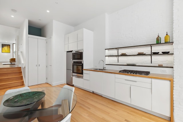 kitchen with white cabinets, a sink, light wood-style floors, stainless steel appliances, and butcher block counters