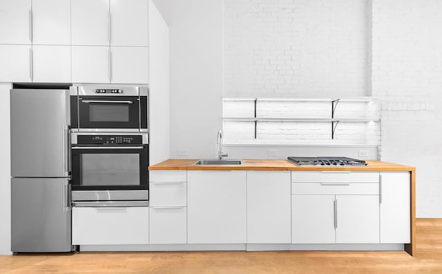 kitchen with a sink, stainless steel appliances, butcher block countertops, and white cabinetry