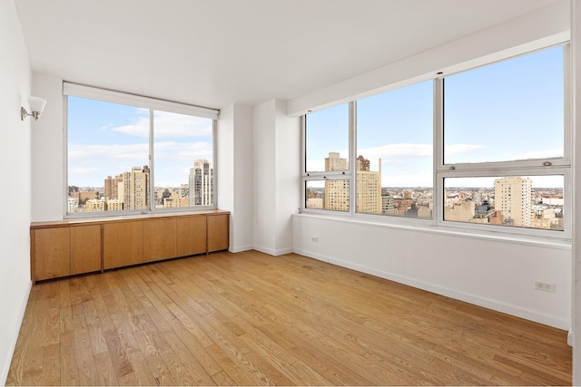unfurnished room with baseboards, a view of city, and light wood finished floors
