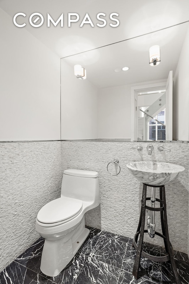 bathroom with a sink, tile walls, toilet, and marble finish floor