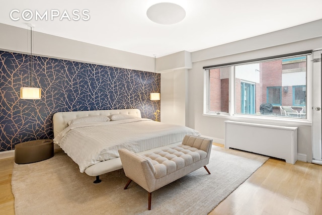 bedroom featuring radiator, an accent wall, wood finished floors, baseboards, and wallpapered walls