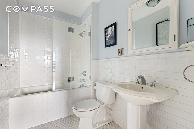 bathroom with wainscoting, toilet, tile patterned floors, tile walls, and tiled shower / bath combo