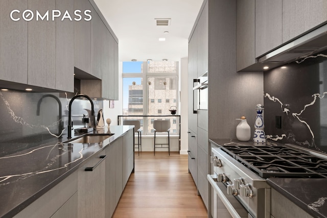 kitchen featuring a sink, light wood finished floors, high end range, visible vents, and modern cabinets