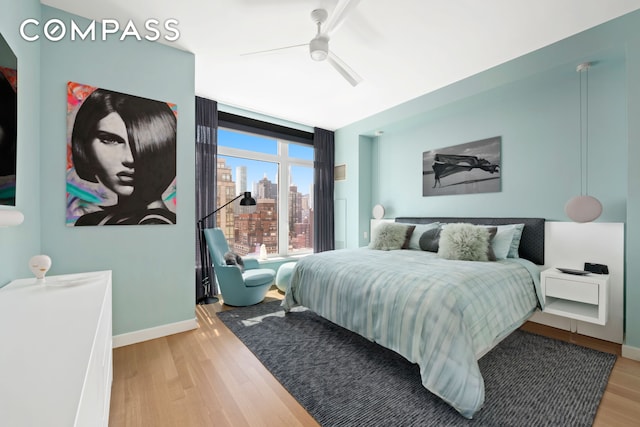 bedroom with a wall of windows, ceiling fan, light wood-type flooring, a view of city, and baseboards