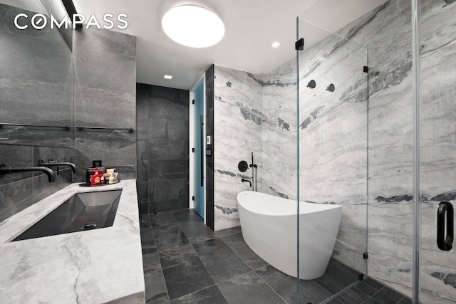full bathroom with a sink, double vanity, tile walls, a soaking tub, and a stall shower