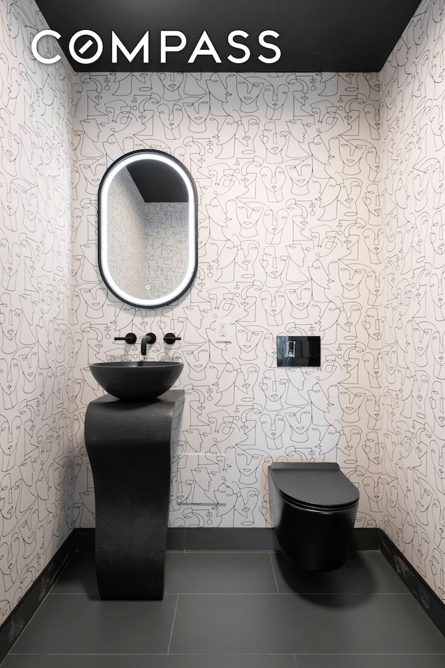 half bathroom with tile patterned flooring, toilet, baseboards, wallpapered walls, and a sink