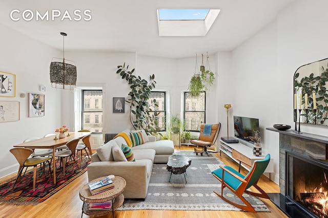 living area featuring baseboards, a skylight, a fireplace with flush hearth, and wood finished floors
