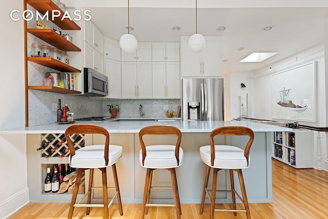 kitchen featuring appliances with stainless steel finishes, tasteful backsplash, open shelves, light countertops, and light wood finished floors