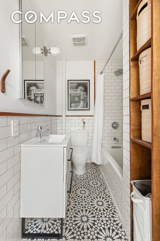 full bathroom featuring visible vents, tile walls, vanity, toilet, and shower / bath combo with shower curtain
