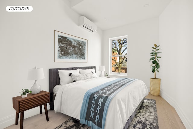 bedroom with baseboards, light wood-style flooring, and a wall mounted air conditioner