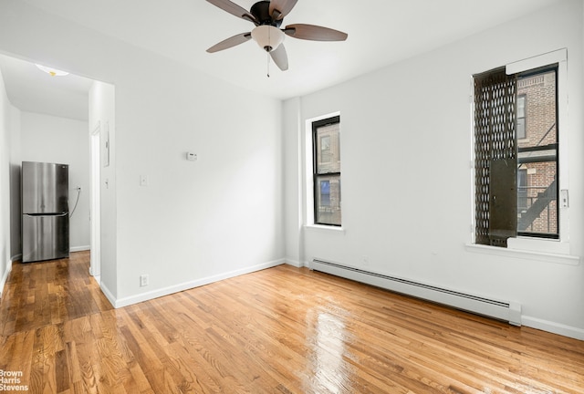 spare room with baseboards, ceiling fan, wood finished floors, and a baseboard radiator