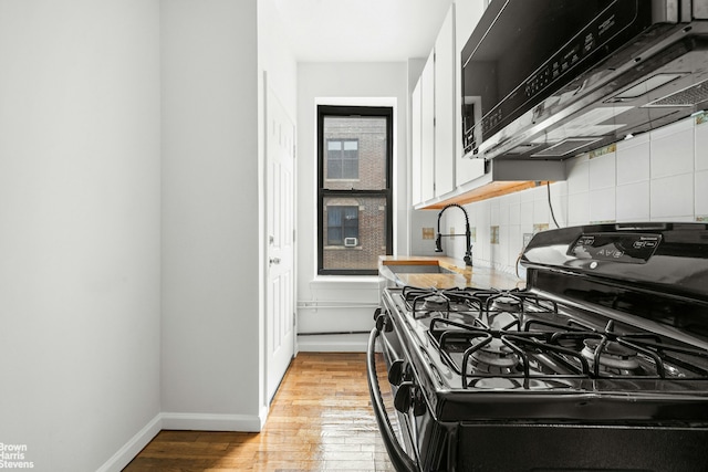kitchen with tasteful backsplash, white cabinetry, a sink, black gas range oven, and light wood-style flooring