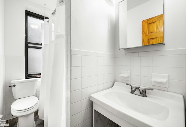 bathroom with a sink, toilet, a shower with shower curtain, a wainscoted wall, and tile walls