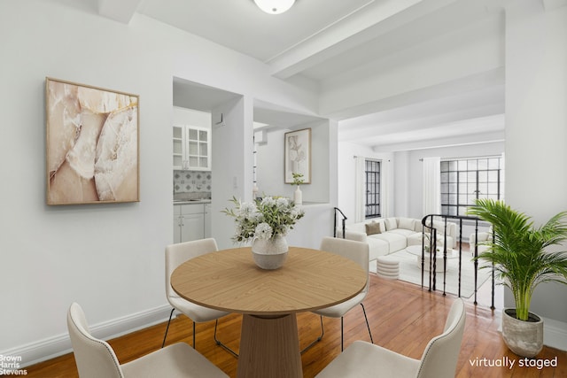 dining space featuring baseboards, wood finished floors, and beam ceiling