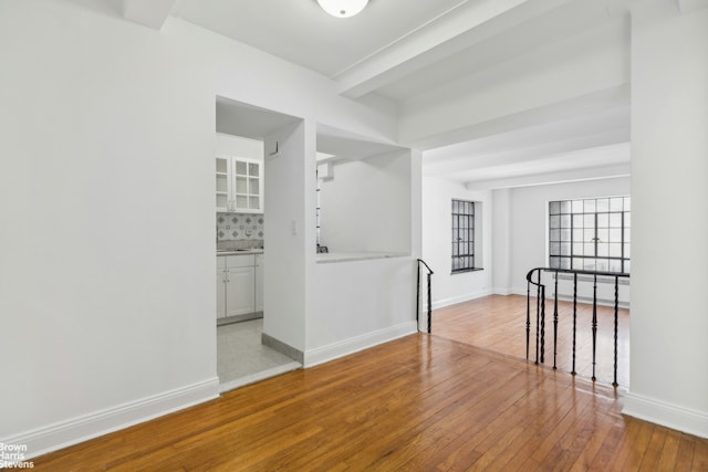 spare room with wood-type flooring, baseboards, and beam ceiling