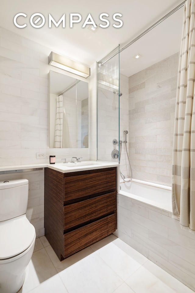 bathroom featuring tile patterned flooring, vanity, toilet, tile walls, and tiled shower / bath
