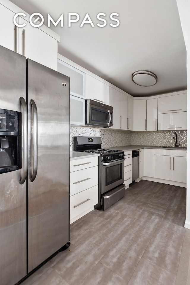 kitchen featuring tasteful backsplash, a sink, white cabinets, glass insert cabinets, and stainless steel appliances