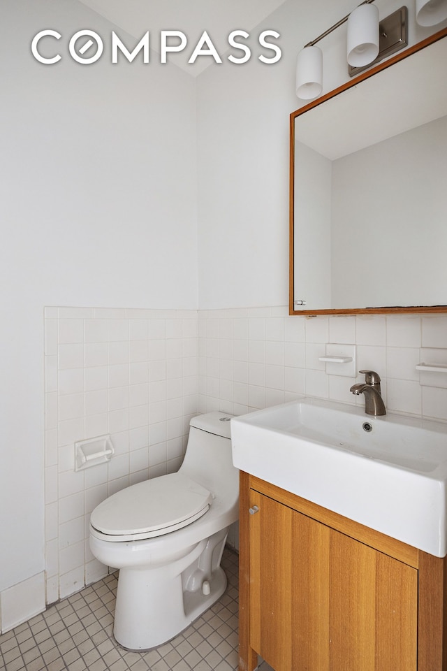 half bath featuring toilet, tile patterned floors, tile walls, and vanity