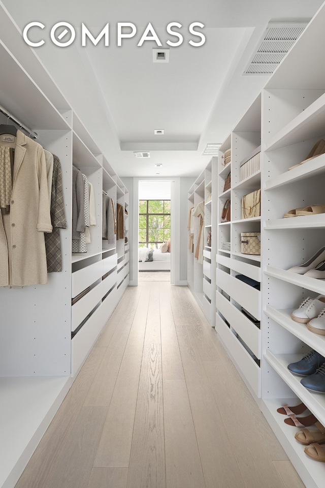 walk in closet featuring light wood-style floors, a tray ceiling, and visible vents